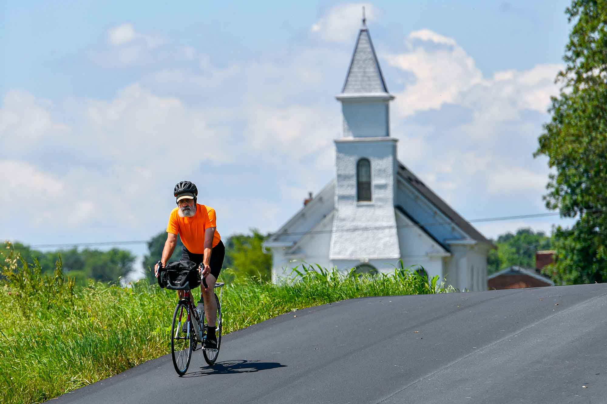 A cyclist rides on a quiet country road near a quiet country church.